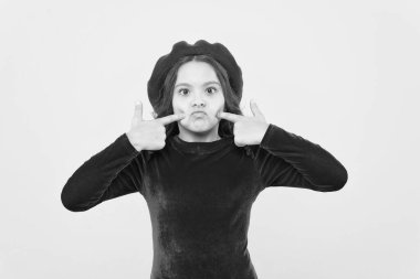 Fransız bereli komik Paris 'li kız surat yapıyor ve sarı arka planda yanakları işaret ediyor, eğleniyor.