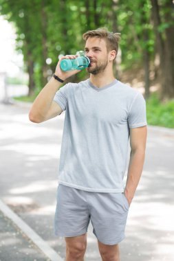 Uzun antrenman bitti. Atletik görünüşlü bir adam şişeyi suyla tutar. Sporcu güneşli bir günde parkta antrenmandan sonra su içer. Sportif giysiler içindeki erkek sporcu ferahlatıcı maden suyu içer.