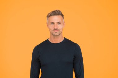 Onun yakışıklı olduğunu biliyor. Olgun bir adamın yakışıklı görünüşü. Yakışıklı adam sarı arka plan. Sıradan bir tarz. Moda trendleri. Erkekler tımar ediliyor. Cilt rutini. Berber dükkanı. Tıraşsız ama yakışıklı.