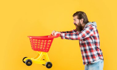 Havalı saç stili olan şık sakallı adam kareli gömlek giyer alışveriş arabası alır.