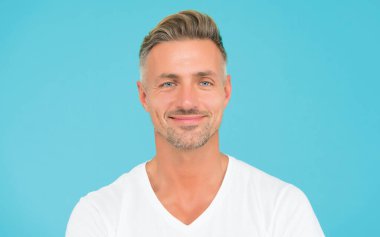 Son moda saç stili ile gülümseyen adam gri saçlı ve turkuaz arka planda bakımlı bir yüze sahip.