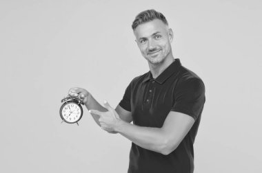 Yakışıklı beyaz adam mekanik çalar saati işaret ediyor. Acil sarı arka plan, son teslim tarihi.