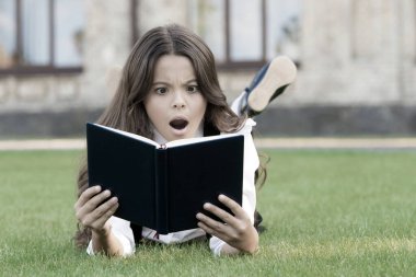 Ders dışı okumalar. Dışarıda kitap okuyan şirin küçük bir çocuk. Temel eğitim. Sevimli küçük kız okumayı öğreniyor. Konsept çalışıyorum. Okul üniforması en sevdiği kitapla çimlerin üzerinde yatıyor.