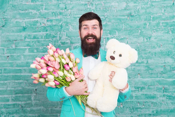 Nice bouquet. Flower for March 8. Love date. international holiday. Bearded man with tulip bouquet and bear. Womens day. Spring gift bouquet. Bearded man hipster with flower bouquet