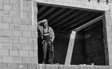 İnşaatta günlük rutin. İyi iş çıkardın. Tamirci inşaat alanında dinlenirken yoruldu. Sigara içen bir inşaatçı. Kır ve rahatla. Sakallı, mühendis üniformalı ve kasklı bir adam. Düzenli gün