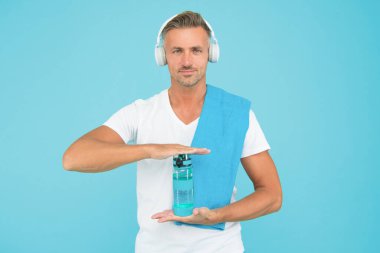 Su içmek fitness hedeflerine ulaşmanın anahtarıdır. Sağlıklı içme alışkanlıkları. Kulaklıklı yakışıklı adam bir şişe içme suyu tutuyor. Daha iyi susuzluk için su içmek. Sunum ve reklam