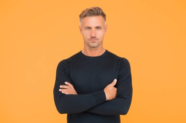 Yakışıklı, kendine güvenen bir adam ellerini çapraz yapmış şık bir saç şekli ve sarı arka planda tüylü bir yüzü var.