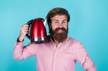 Bunu denemelisin. Mutfak konsepti Bıyıklı vahşi yakışıklı adam çay içiyor. Olgun koca elektrikli su ısıtıcısı tutar. Hayattaki modern teknoloji. Sakallı hippi ev aletleri kullanıyor.