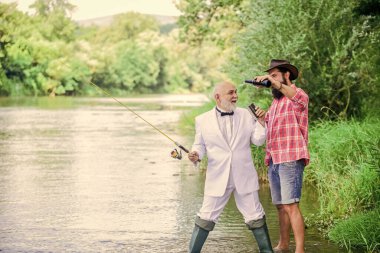 Sakallı adam ve zarif iş adamı birlikte balık tutuyor. Erkekler doğayı rahatlatıyor. Eğlen ve rahatla. Hafta sonu tatili. Balık tutma becerileri. Oltayı oltaya getirin. Balık tutmak ve bira içmek.
