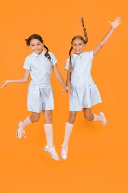Eğleniyorum. Eski moda. Klasik tarzda çocuklar. Eski usul. Mutlu arkadaşlar sarı arka planda zıplarlar. Çocuk modası güzeli. çocukluk mutluluğu. Kardeşlik kavramı. Okul üniformalı küçük kızlar
