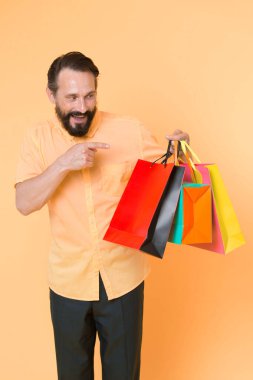 Alışveriş mutluluğu. Alışverişten zevk alan bir adam. Sarı arka planda alışveriş torbası olan sakallı olgun bir adam. İndirim ve indirim. İnternetten alışveriş. Kârlı bir alışveriş. Tezgahtar veya satış uzmanı