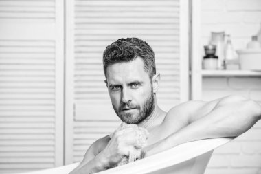 Küvette çıplak maço. Köpüğü dikkatlice suyla yıka. Seks ve rahatlama konsepti. Maço, çekici, çıplak adam. Banyodaki seksi adam. Adam kaslı vücudu süngerle yıkıyor. Sabunlu zevk.