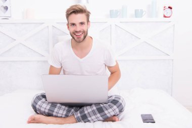 Pijamalı mutlu adam COVID-19 salgını sırasında evde çalışırken bilgisayarını kullanıyor.