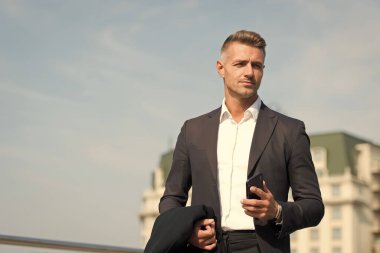 Harekete geçerek karar ver. Mobil iletişim. Başarılı ve motive olmuş bir iş adamı. İş adamı, bakımlı bir saç stili. İş konsepti. İş hayatı. Klasik stil mavi gökyüzü arkaplanı