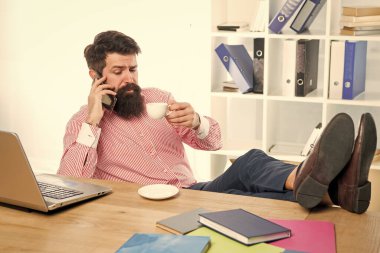 Yönetimde mükemmellik. Müdür telefonda çay içerken konuşuyor. Ofis müdürü masasında dinleniyor. Mobil teknolojiyi kullanarak. İş iletişimi. Modern hayat