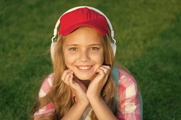 Everything is cool. Cool kid listen to music on green grass. Happy child use headphones outdoors. Cool relaxing music. Calming tunes. New technology for pleasure. Fashion and style. Cool and modern