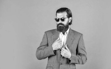 Gri arka planda duran yakışıklı adam. Ciddi sakallı iş adamı. Modern görünümlü şık, olgun bir adam. Erkek ceketi dolabı. Modaya uygun bir adam gözlük takıyor. Resmi manken. Boşluğu kopyala