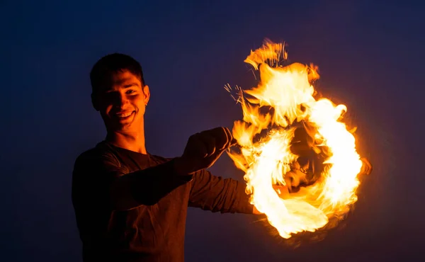 Happy guy artist perform fire circle by spinning burning poi on idyllic dark sky at night outdoors, orbital