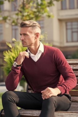 Herkesin kendine biraz zaman ayırmaya ihtiyacı vardır. Yakışıklı adam dışarıda bankta rahatlıyor. Sıradan tarzda çekici bir adam. İş adamının modaya uygun görünüşü. Moda ve tarz. Sıradan erkek kıyafetleri.