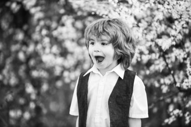 Neşe dolu. Mutlu çocuğun gür ve sağlıklı saçları var. Yaz ve bahar modası. Çocuk kısmen doğanın çiçeklenmesinden hoşlanıyor. çocukluk mutluluğu. Kaygısız çocuk baş parmağını kaldırdı. Çiçek açan bahar ağacında küçük bir çocuk