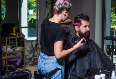 Berber dükkanına gelen olgun, beyaz bir adam bir kuaför, kendine bakan, erkeksi bir güzelliğin yardımıyla sakal ve saç getiriyor.