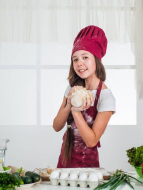 Aşçı çocuk para kazanıyor. Çocuk evde sağlıklı yemekler hazırlar ve aşçı üniforması giyer. Oda servisi ve ev işleri. Çocukluk gelişimi. Küçük kız mutfakta yemek pişiriyor. Mutfak eşyaları.