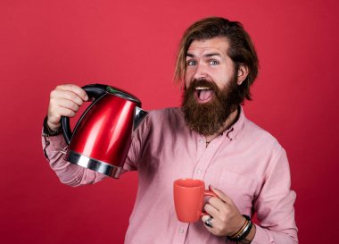Çay içme zamanı konsepti. Gömlekli sakallı adam elektrikli su ısıtıcısı tutuyor. Sıradan bir adam modern teknolojiyi günlük hayatta kullanır. Bıyıklı mutlu hipster, kaynar su. erkek evi.