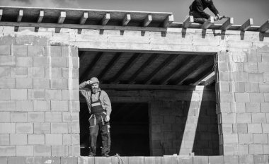Üniformalı ve kasklı sakallı adam. Tamirci olay yerinde kask takıyor. Yorgun müteahhit. Sigara içen inşaat işçisi. Bina yapım aşamasında.