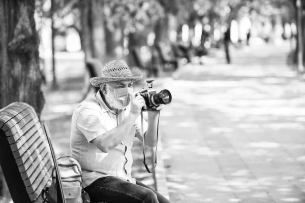 old man relax in park. life during coronavirus lockdown. enjoy the beauty. fear of illness. photographer with camera on bench. prohibition on visiting public places. senior man in medical mask