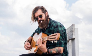 Müzik konsepti. Bıyıklı vahşi yakışıklı adam gitar çalıyor. Olgun müzisyen ve şarkıcı. Sıradan stil gitarist. Modern görünümlü sakallı, akustik gitarlı hippi. Düşürenleri yener