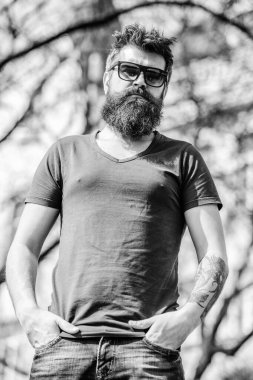 Güneş gözlüklü, sakallı, doğa geçmişi olan bir adam. Sakallı adam modern güneş gözlüğü takıyor. Hippi koyu güneş gözlüklerine güveniyor. UV filtresi. Sakallı hippi vahşi adam koruyucu güneş gözlüğü takıyor.