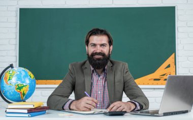 Sakallı ve bıyıklı bir adam üniversitede ya da okulda iş adamı ya da öğretmen gibi görünüyor.