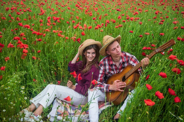 Casal romântico tocando guitarra em um campo com flores vermelhas, férias de verão — Fotografia de Stock