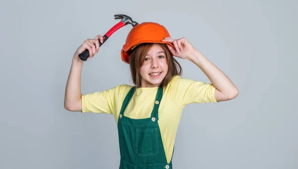 調べます。改修と修理です。作業道具を使って。ヘルメットを着た10代の女の子とハンマーでボイラースーツ。子供は硬い帽子をかぶる。建設現場の子供のビルダー。労働者技術者。建築家がワークショップで — ストック写真