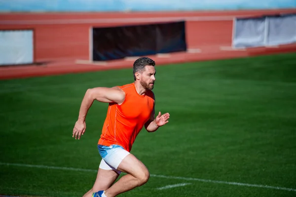Enérgico atlético hombre musculoso corredor corriendo al aire libre sobre hierba verde, resistencia — Foto de Stock