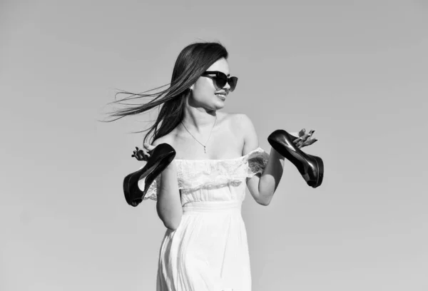 Liberdade. Menina em óculos de sol espaço de cópia. Modelo tenra vestido de verão. Para o verão. Conceito de Afterparty. Mulher nascer do sol carrega saltos altos na mão. Mulher no céu azul ensolarado da manhã. Férias de verão — Fotografia de Stock