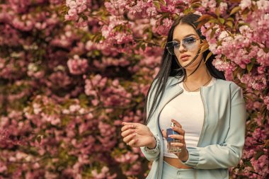 Uzun süreli etki. Parfüm markası. Aroma bileşikleri. Şatafatlı bir koku. Modaya uygun bir kadın parfüm şişesi tutuyor. Kiraz çiçeği aroması. Kadın parfümü. Bahar parfümü. Süslü bir tarz. Hoş bir koku ver