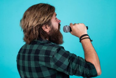 Olgun sakallı adam mikrofonla şarkı söyleyerek modaya uygun görünüyor.