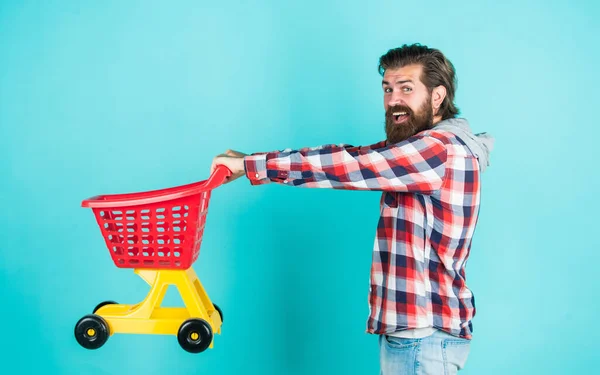 Kareli tişörtlü, olgun, yakışıklı bir adam alışveriş arabası taşıyor ve satın alıyor. — Stok fotoğraf