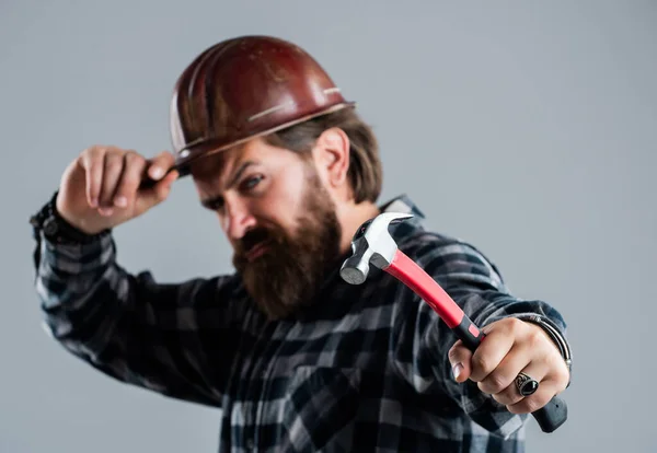Бородатый хипстер в клетчатой рубашке и шлеме рабочего, избирательный фокус, молоток — стоковое фото