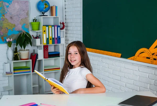 Smiling teen girl reading book in school classroom, education — Stock Photo, Image