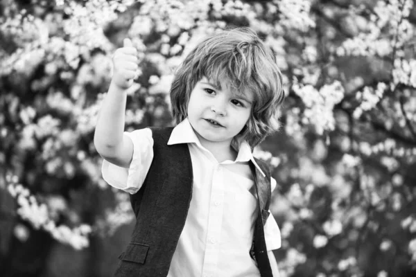 Petit garçon à l'arbre de printemps en fleurs. enfant heureux a des cheveux sains luxuriants. été et printemps mode. enfant profiter de la floraison de la nature en partie. bonheur d'enfance. insouciant garçon montrer pouce vers le haut — Photo