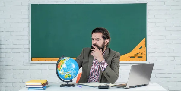 mature bearded man teacher in costume sit in school classroom with geography globe map, location