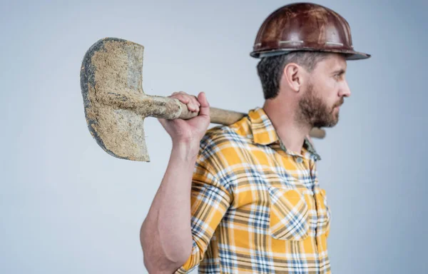 Schaufel in der Hand des Arbeiters. Typen tragen Arbeiteruniform. Schöner Bauarbeiter mit Helm. — Stockfoto