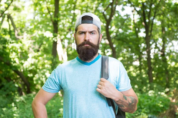 Maturo uomo barbuto con barba e baffi in camicia estiva e berretto tenere zaino nella foresta, viaggiatore — Foto Stock