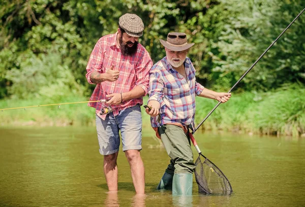 Que tem mais. pesca de pai e filho. hobby e atividade esportiva. Isca de truta. dois pescadores felizes com vara de pesca e rede. Fim de semana. homens maduros pescador. amizade masculina. ligação familiar — Fotografia de Stock