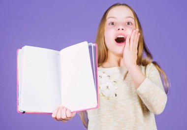 Kütüphanedeki sınavlara hazırlanıyorum. Küçük mutlu çocuk açık bir kütüphane kitabı tutuyor. Kitapla gülümseyen sevimli küçük kütüphane okuyucusu. Okul kütüphanesinde okumak, kopyalama alanı