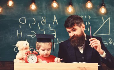 Hometask konsepti. Sınıfta havan tahtasındaki resmi giyim ve öğrenci öğretmeni, arka planda yazı tahtası. Hevesli çocuk öğretmeniyle ders çalışıyor. Baba sorguyu kontrol ediyor, çocuğa yardım ediyor, evlat