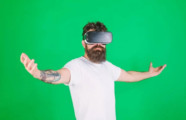 A felsőbbrendűség fogalma. Hipster komoly arcfelemelő kezét, miközben élvezze a fölényét a virtuális valóságban. A fejre szerelt kijelzős fickó kölcsönhatásba lép a VR-rel. Szakállas férfi VR szemüvegben, zöld háttér — Stock Fotó