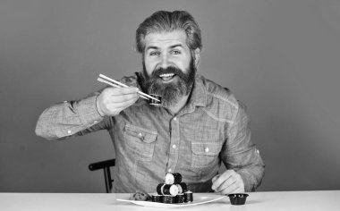 Evde akşam yemeği. hipster yemek çubuklarıyla suşi yer. Lezzetli suşi rulosu. Japonya 'da geleneksel ve sağlıklı yiyecekler. Japon suşi yemeği. Geleneksel Japon yemeklerini çubuklarla yiyen adam.